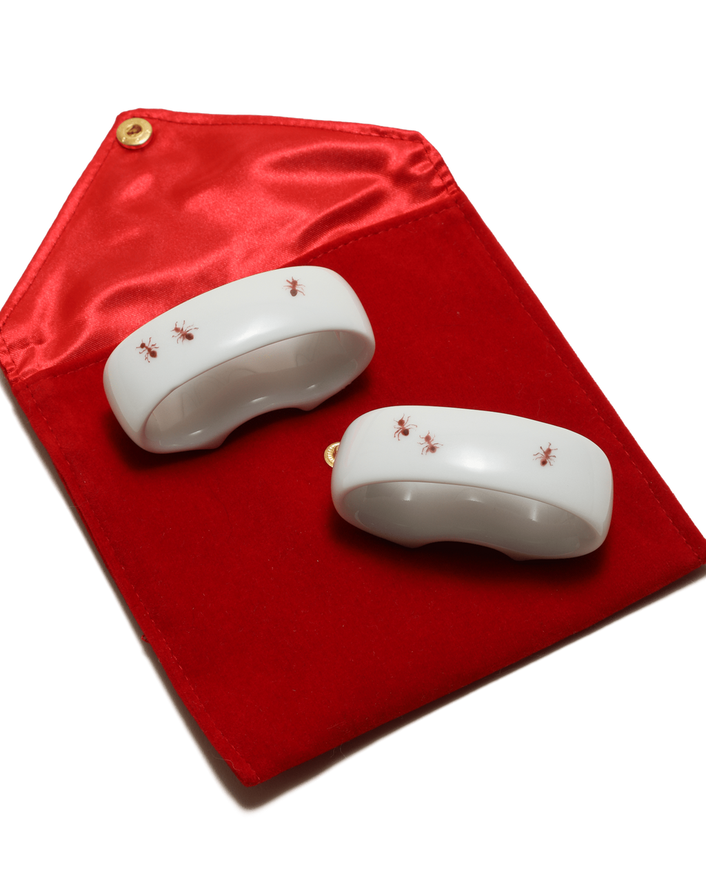 Two white ceramic items with red ants painted on a red fabric background