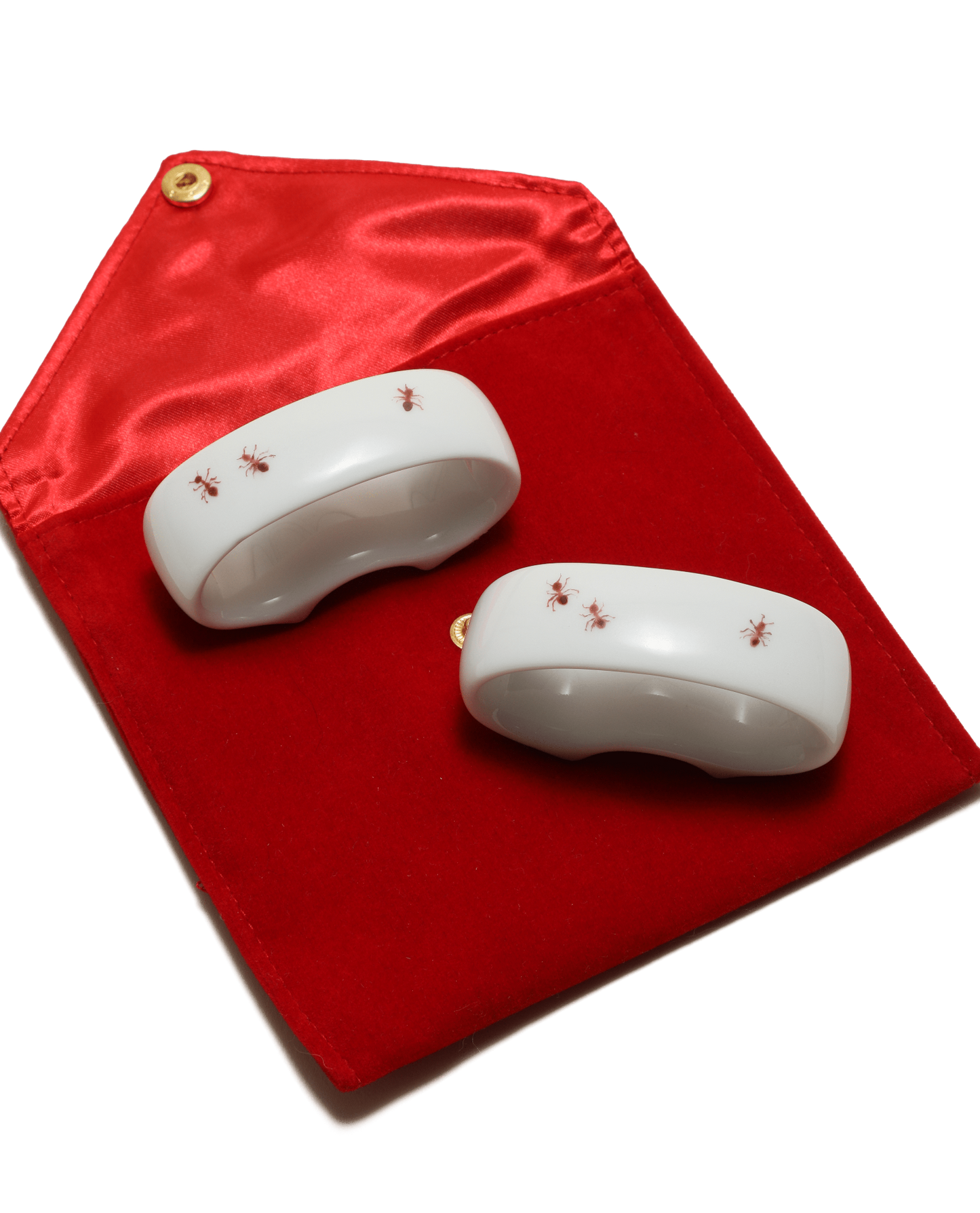 Two white ceramic items with red ants painted on a red fabric background