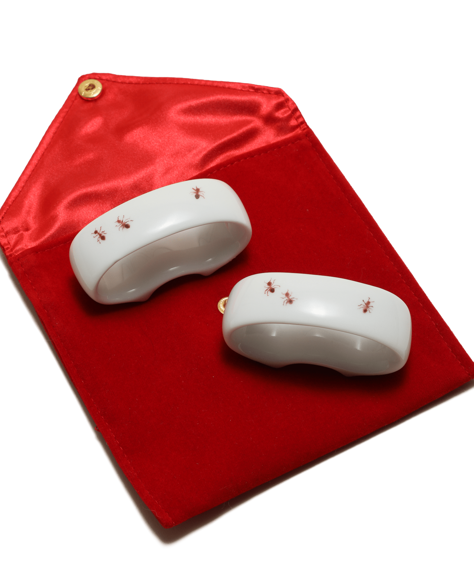 Two white ceramic items with red ants painted on a red fabric background